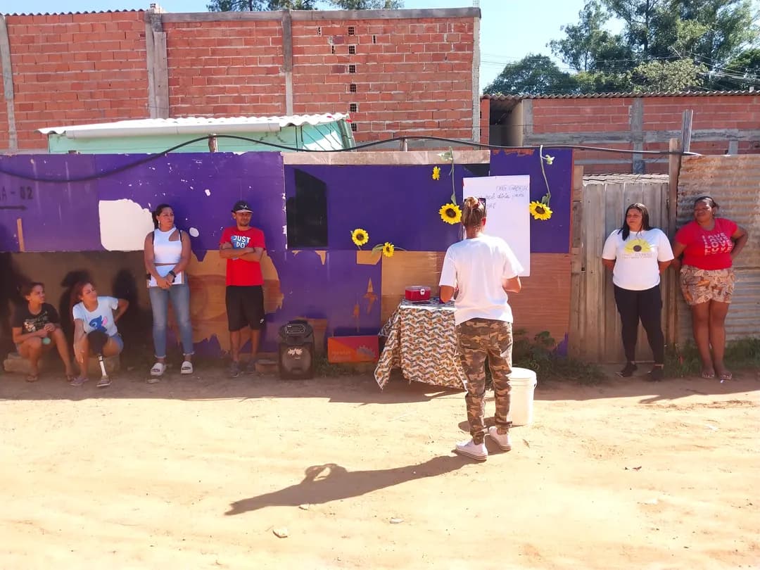 Ação ao ar livre no bairro, com crianças e adultos diante de um painel roxo decorado com girassóis.