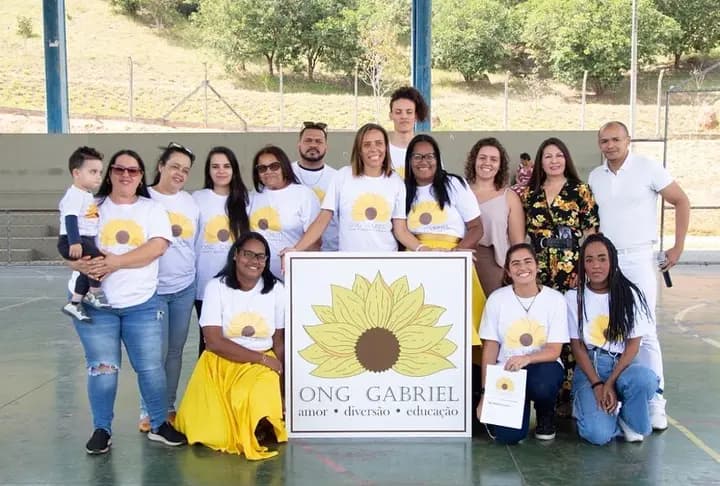 Equipe da ONG Gabriel reunida ao redor do cartaz com o girassol e o nome da ONG.