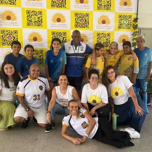 Voluntárias da ONG Gabriel com crianças e adolescentes em frente ao painel de girassóis.